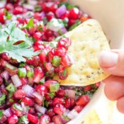 Closeup of fingers dipping a yellow tortilla chip into a serving bowl filled with this salsa recipe.