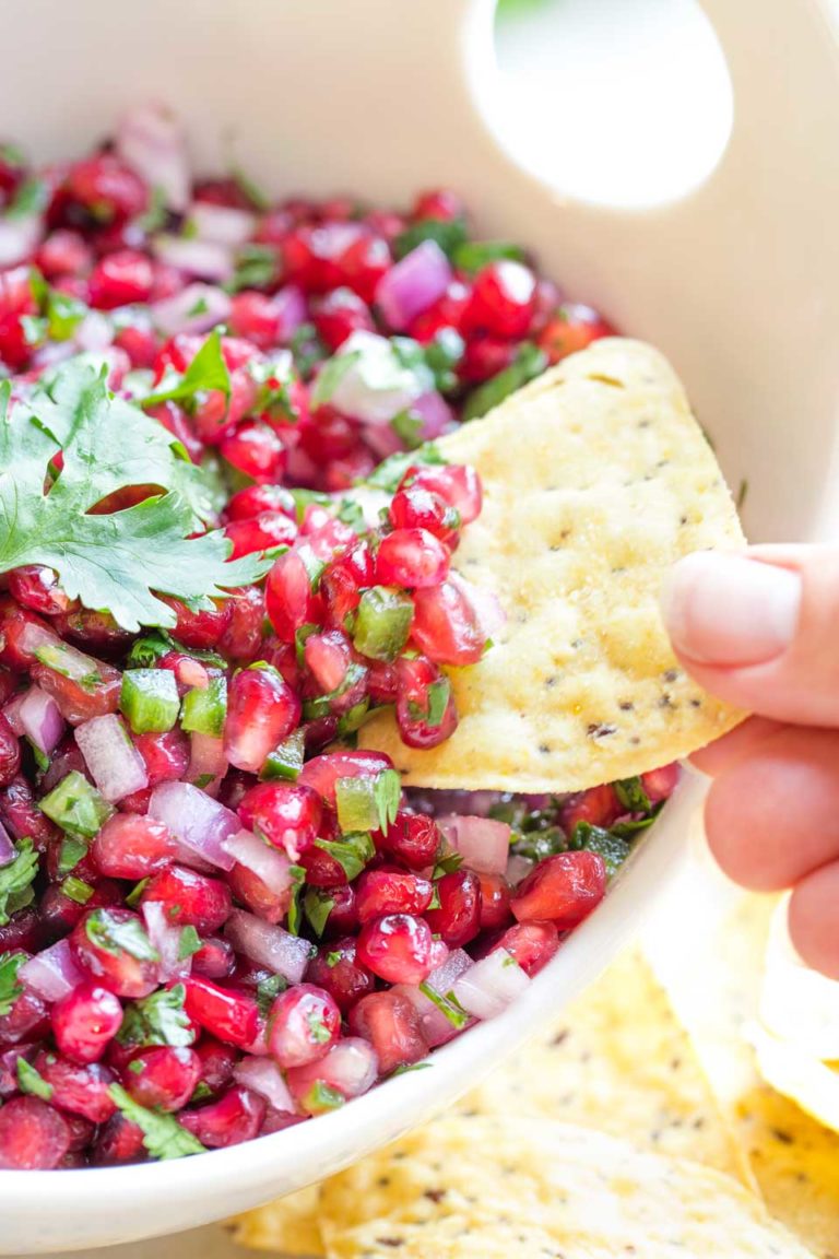 Closeup of fingers dipping a yellow tortilla chip into a serving bowl filled with this salsa recipe.