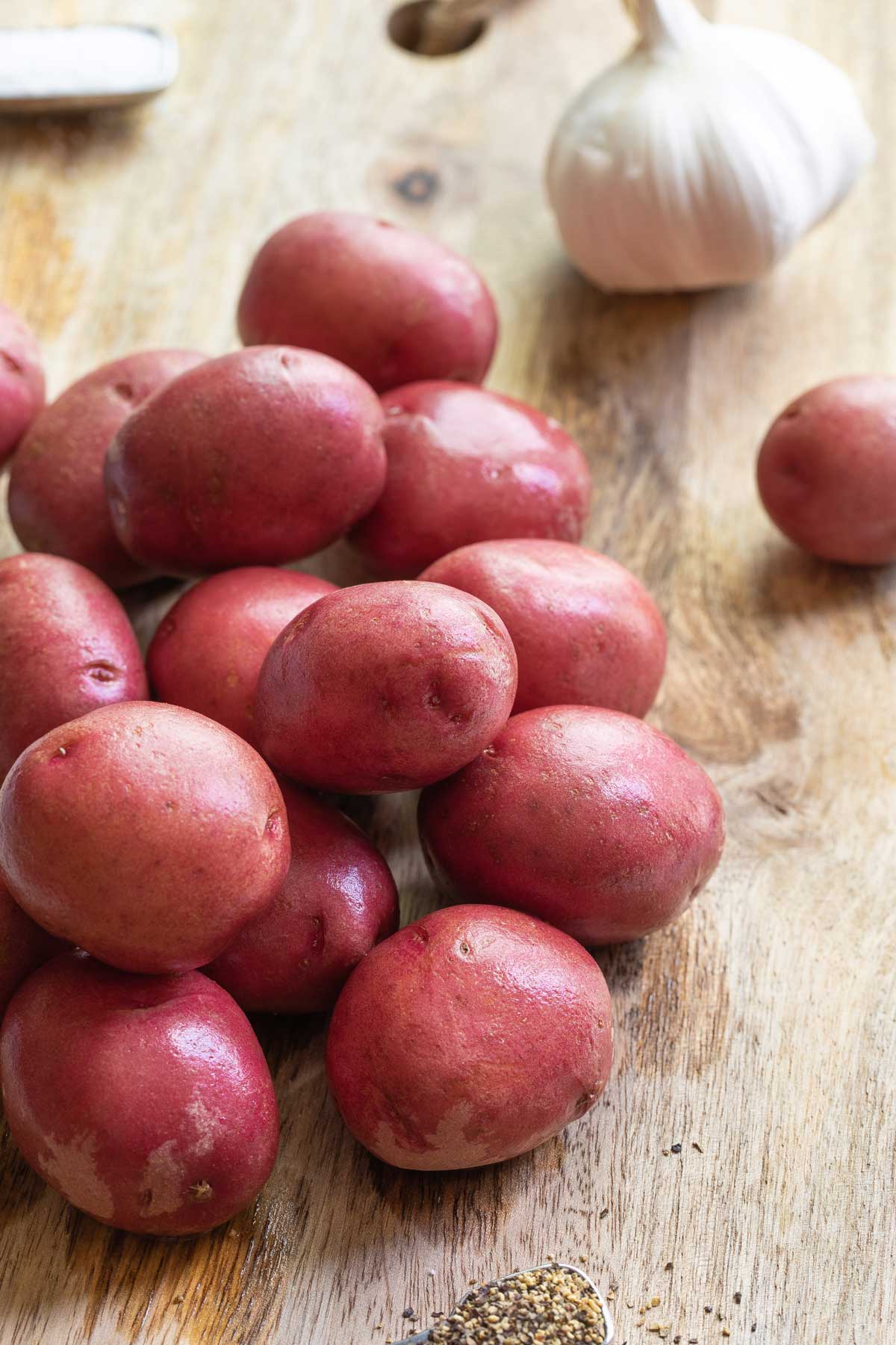 Pile of whole red potatoes on cutting board with head of garlic in background.