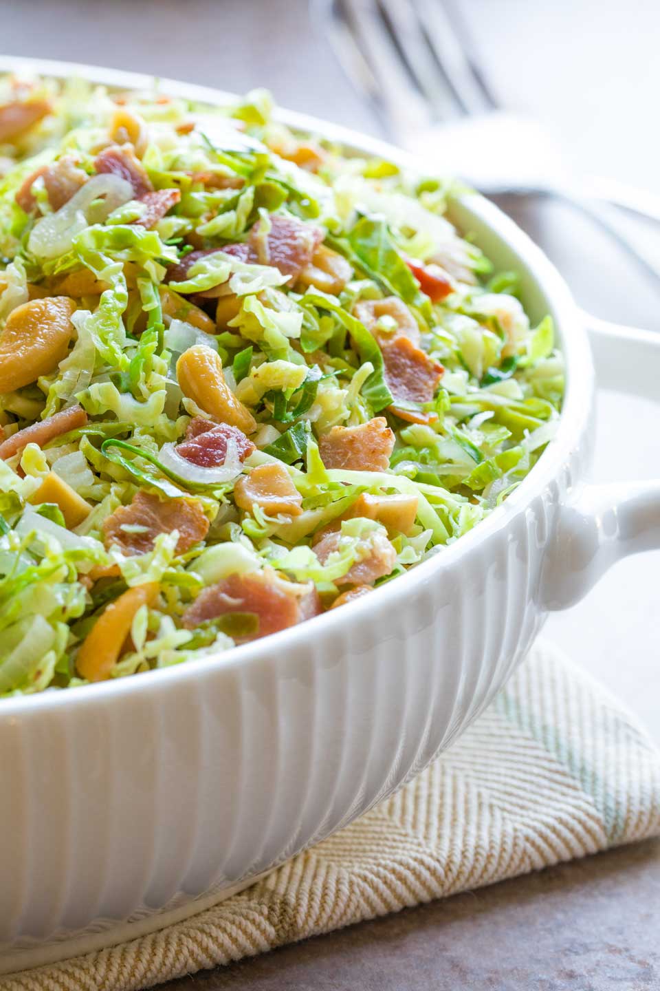 Side view of white ridged serving dish so you can really see the bits of Brussel sprouts and bacon and cashews.