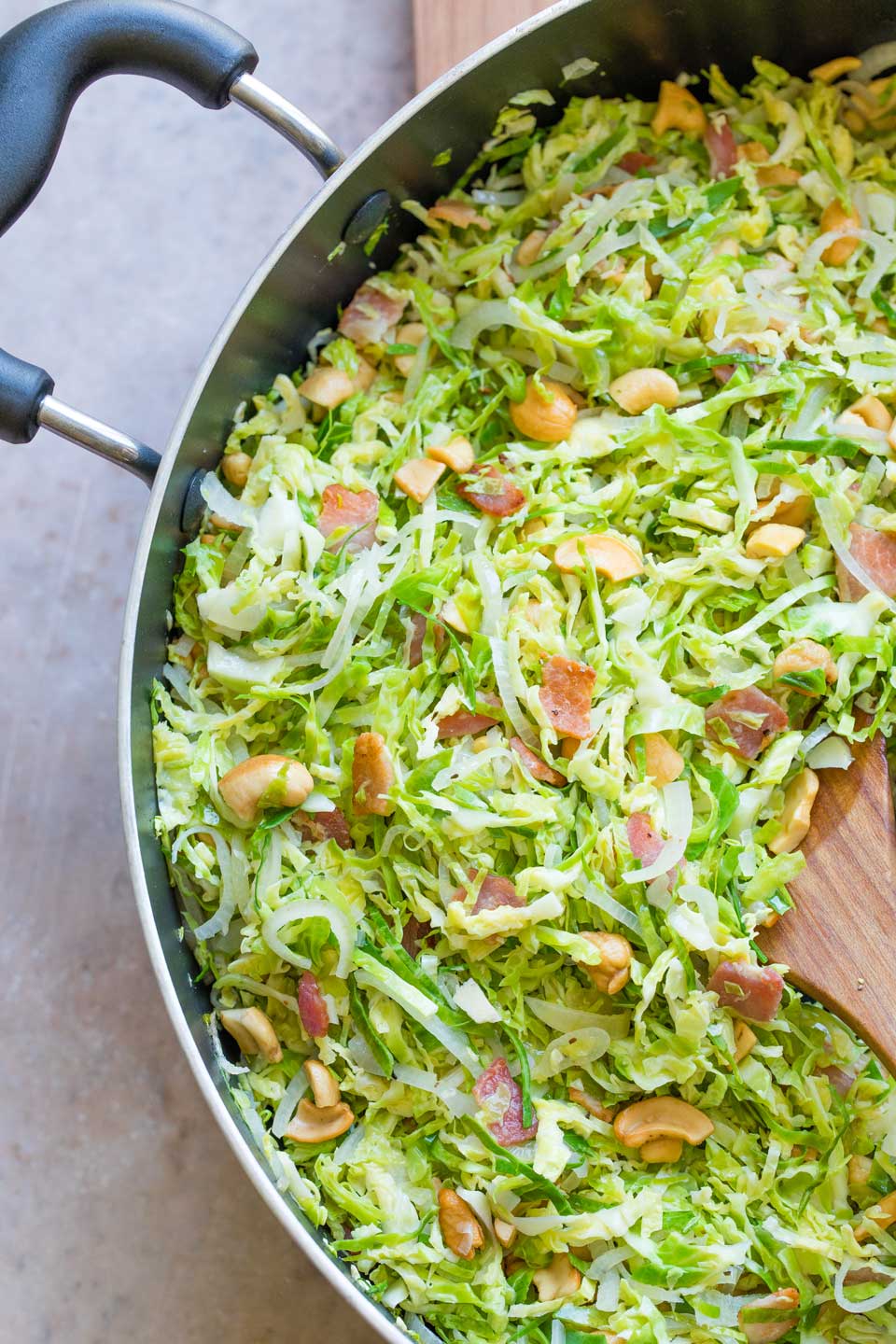 Overhead closeup of sauteed Brussel sprouts and bacon, still in pan, with wooden spoon.