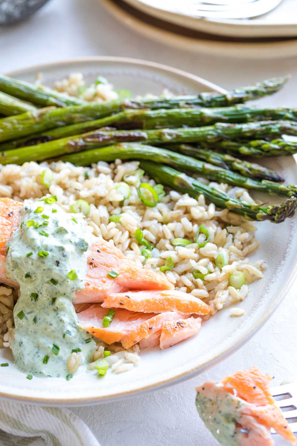 Plated meal with the salmon on a bed of rice with asparagus spears, with a fork to the side having just flaked away the first bite of salmon.