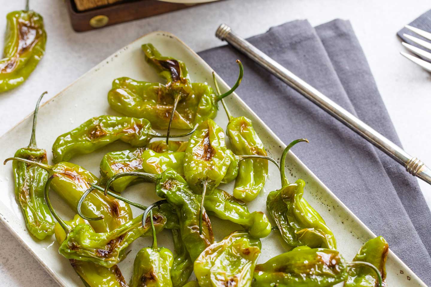 Closeup of cooked peppers on rectangular, cream serving platter on grey cloth.