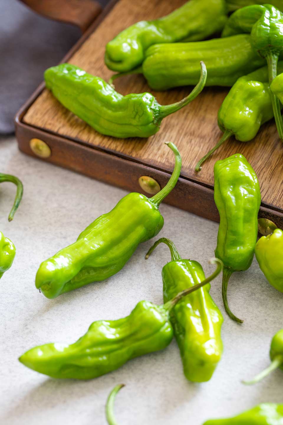 Uncooked shishito peppers cascading off a serving board.