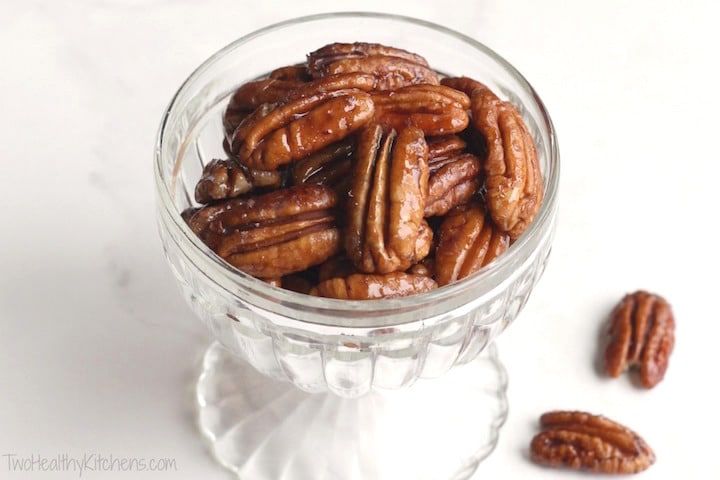Glass parfait dish filled with candied pecans, with two extras lying next to it.
