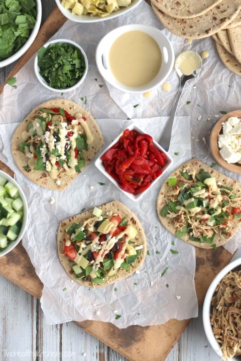 Flatlay of 3 tacos piled with chicken and different topping combinations, with extra toppings surrounding.