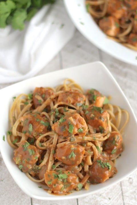 One serving of salmon pasta in square bowl with a large white serving dish of more pasta in background.