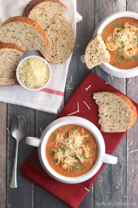 Flatlay scene of 2 bowls filled with tomato soup, with and red cloths, bread slices and dish of parmesan.