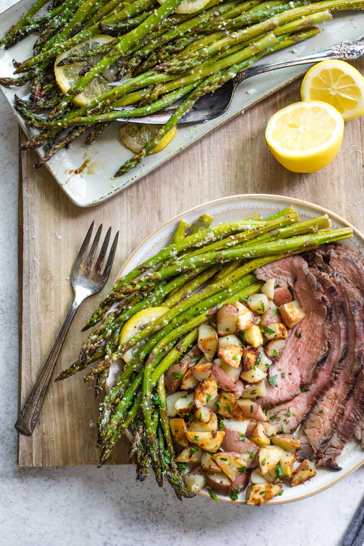 Plated dinner of grilled asparagus, potatoes and steak with serving platter of asparagus nearby.